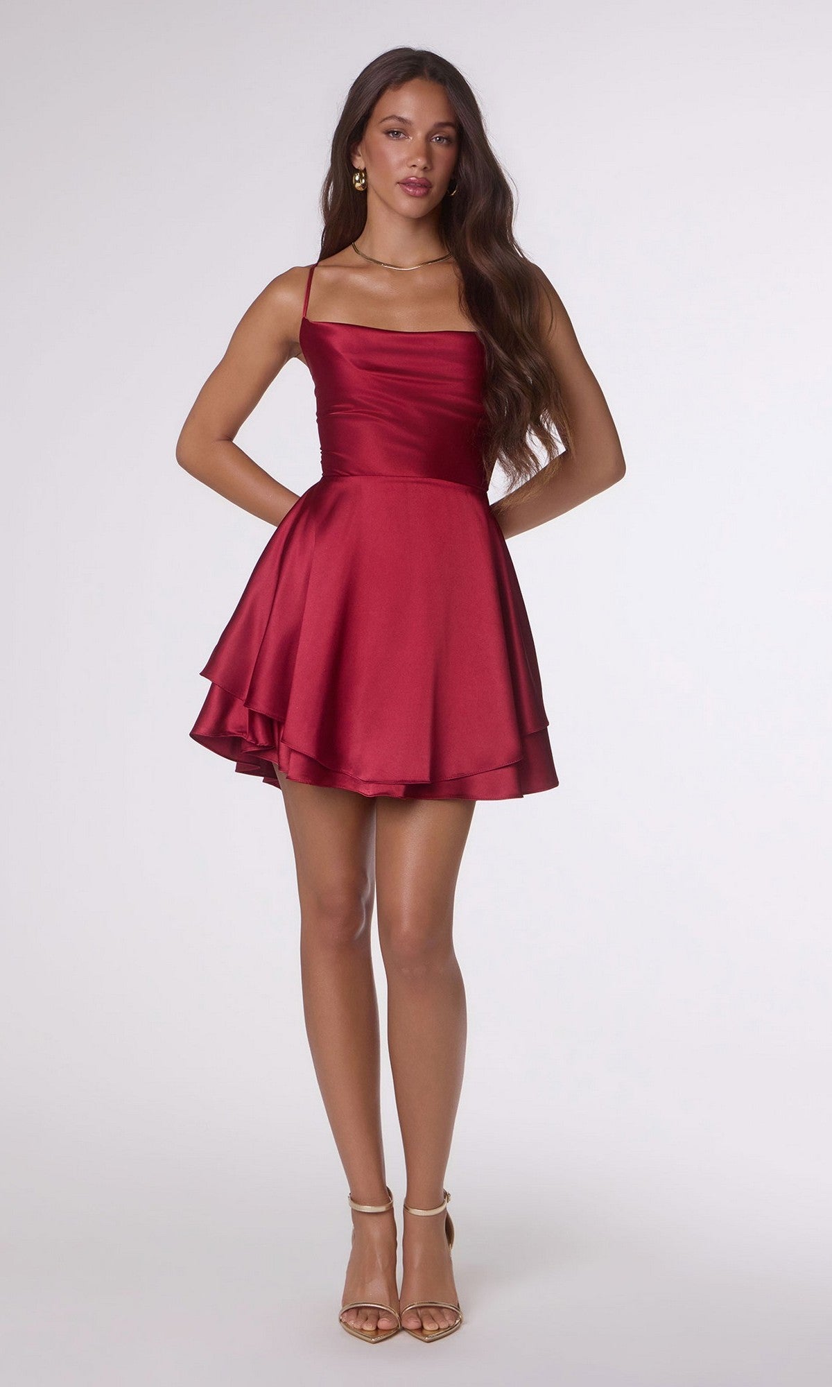 A woman wears the Amoris T616 short homecoming dress, featuring a sleeveless red satin design with an A-line skirt and fitted bodice, styled with nude high-heeled sandals.
